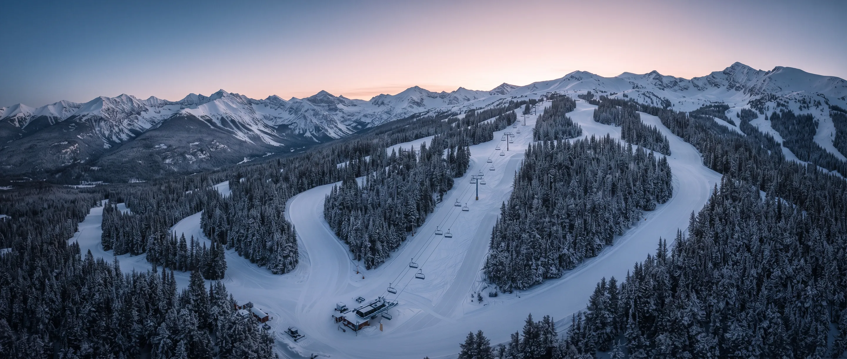 Dawn light over a ski resort's groomed trails, chairlift, and mountain peaks